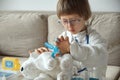 Little doctor in medical coat with stethoscope play bandage to teddy bear toy Royalty Free Stock Photo