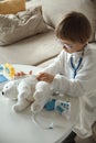 Little doctor in medical coat with stethoscope play bandage to teddy bear toy Royalty Free Stock Photo