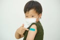 Little doubtful kid wearing medical mask showing his arm with bandage after receiving vaccination Royalty Free Stock Photo