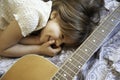 Little dreamer girl lying on the bed with her acoustic guitar. She`s smiling with hand on the face. She`s joking with her guitar Royalty Free Stock Photo