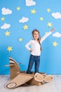 Little dreamer girl playing with a cardboard airplane at the studio with blue sky and white clouds background. Royalty Free Stock Photo