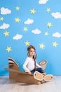 Little dreamer girl playing with a cardboard airplane at the studio with blue sky and white clouds background. Royalty Free Stock Photo