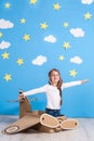 Little dreamer girl playing with a cardboard airplane at the studio with blue sky and white clouds background. Royalty Free Stock Photo