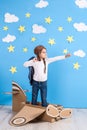 Little dreamer girl playing with a cardboard airplane at the studio with blue sky and white clouds background. Royalty Free Stock Photo