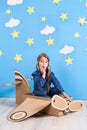 Little dreamer girl playing with a cardboard airplane at the studio with blue sky and white clouds background. Royalty Free Stock Photo