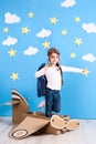 Little dreamer girl playing with a cardboard airplane at the studio with blue sky and white clouds background. Royalty Free Stock Photo