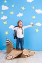 Little dreamer girl playing with a cardboard airplane at the studio with blue sky and white clouds background. Royalty Free Stock Photo