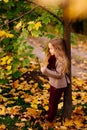 Little dreamy girl is standing under tree in autumn Park with bird feather