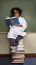 Little Einstein. A cute young ethnic boy wearing a labcoat and glasses sitting on a stack of books reading.