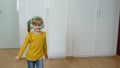 Little child girl wearing headphones listening to music and funnily dancing near wardrobe at home