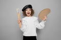 Emotional little girl artist poses in studio holds paintbrushes and palette. Children hobby concept Royalty Free Stock Photo