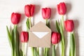 Little envelope on red tulips on white wooden background. Flat lay with copy space Royalty Free Stock Photo