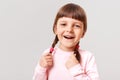 Little European cute laughing girl in casual jumper looking diretcly at camera, touching her pigtails, laughing happily isolated