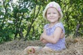 Little farm girl sitting on natural cereal straw bale at green tree leaves summer background Royalty Free Stock Photo