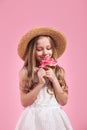 Little fashion beauty girl in straw hat smelling flower on pink background