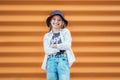 Little fashion-dressed girl portrait sincerely smiling while looking at camera on orange wall background. Urban people living and