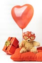 Little fluffy teddy bear wearing red heart shaped glasses and holding red balloon. Happy Valentine\'s Day. Presents in a red Royalty Free Stock Photo