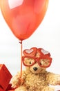 Little fluffy teddy bear wearing red heart shaped glasses and holding red balloon. Happy Valentine\'s Day. Presents in a red Royalty Free Stock Photo