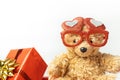 Little fluffy teddy bear wearing red heart shaped glasses and holding red balloon. Happy Valentine\'s Day. Presents in a red Royalty Free Stock Photo