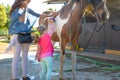 Little girl brushing a horse with her mother next to stables Royalty Free Stock Photo