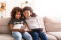 Little friends using gadgets, playing games on sofa Royalty Free Stock Photo