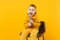 Little fun kid boy 3-4 years old in yellow clothes sing song in microphone isolated on bright orange wall background Royalty Free Stock Photo