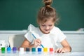 Little funny artist painting, drawing art. Child girl draws in classroom sitting at a table, having fun on school Royalty Free Stock Photo