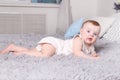 Little funny baby in white lies on bed with pillows