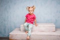 Little funny blue-eyed girl child blonde with a haircut two ponytails on her head sitting on a gossip on the background of an old Royalty Free Stock Photo