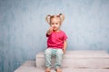 Little funny blue-eyed girl child blonde with a haircut two ponytails on her head sitting on a gossip on the background of an old Royalty Free Stock Photo