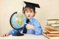 Little funny boy in academic hat showing on the globe among old books Royalty Free Stock Photo