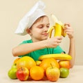 Little funny boy peeling fresh banana at table with fruits Royalty Free Stock Photo