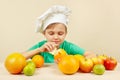 Little funny boy peeling fresh orange at table with fruits Royalty Free Stock Photo