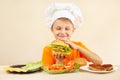 Little funny chef in chefs hat enjoys cooking tasty hamburger Royalty Free Stock Photo
