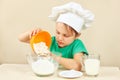 Little funny chef pours flour for baking cake