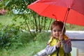 little funny cute girl walks in the rain with a red umbrella, in green rubber boots through the puddles. Laughs, has fun Royalty Free Stock Photo