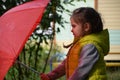 little funny cute girl walks in the rain with a red umbrella, in green rubber boots through the puddles. Laughs, has fun Royalty Free Stock Photo