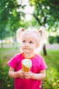 Little funny girl blonde eating sweet blue ice cream in a waffle cup on a green summer background in the park. smeared her face an Royalty Free Stock Photo