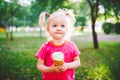 Little funny girl blonde eating sweet blue ice cream in a waffle cup on a green summer background in the park. smeared her face an Royalty Free Stock Photo