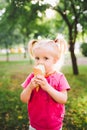 Little funny girl blonde eating sweet blue ice cream in a waffle cup on a green summer background in the park. smeared her face an Royalty Free Stock Photo