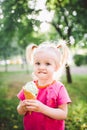 Little funny girl blonde eating sweet blue ice cream in a waffle cup on a green summer background in the park. smeared her face an Royalty Free Stock Photo