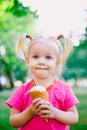 Little funny girl blonde eating sweet blue ice cream in a waffle cup on a green summer background in the park. smeared her face an Royalty Free Stock Photo