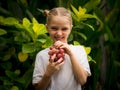 Little funny girl holding bunch of red grapes near her face, showing tongue. Selected focus. Green tropical leaves background. Royalty Free Stock Photo