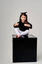 little funny girl sitting on a black cube on a white background