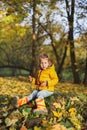 Little funny girl in stylish yellow warm jacket, jeans, orange rubber boots sits on old tree stump in autumn forest or park Royalty Free Stock Photo