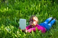 Little funny girl with a tablet makes a self-portrait lying in the green grass.