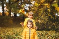 Little funny girls, sisters in stylish yellow raincoat, jacket play in autumn forest or park outdoors, throw up above head old Royalty Free Stock Photo