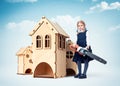 Little funny serious girl in a school uniform with electric saw in her hands stands next to the wooden houses. Construction concep