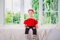 Little funny two years old girl child in stylish red clothes and jeans and sneakers on windowsill near window. With a smile On his Royalty Free Stock Photo