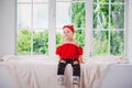 Little funny two years old girl child in stylish red clothes and jeans and sneakers on windowsill near window. With a smile On his Royalty Free Stock Photo